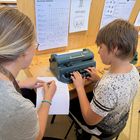 Junge schreibt mit Braille Schreibmaschine. Dadurch entstehen Bilder. In diesem Fall ein Segelschiff.